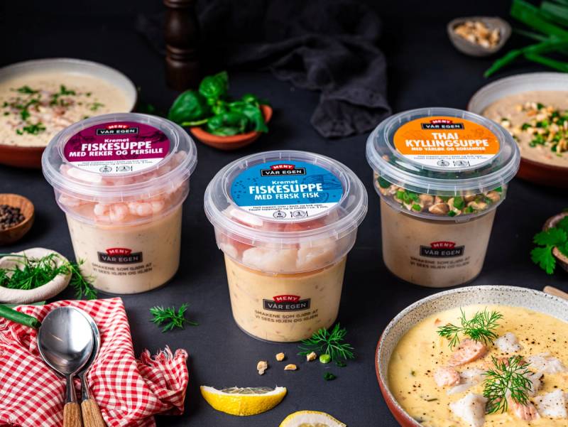 To kopper med fiskesuppe og en skål med kyllingsuppe omgitt av grønnsaker og sitronbiter på et bord.