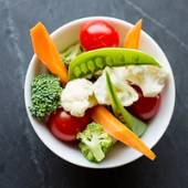 En bolle med ulike rå grønnsaker som tomater, gulrøtter, brokkoli, blomkål og sukkererter.