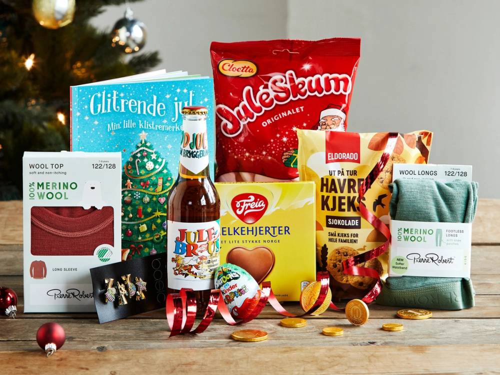 Ulike julegodter og snacks på et bord, inkludert sjokolade, kjeks og godteri, med en julegran i bakgrunnen.