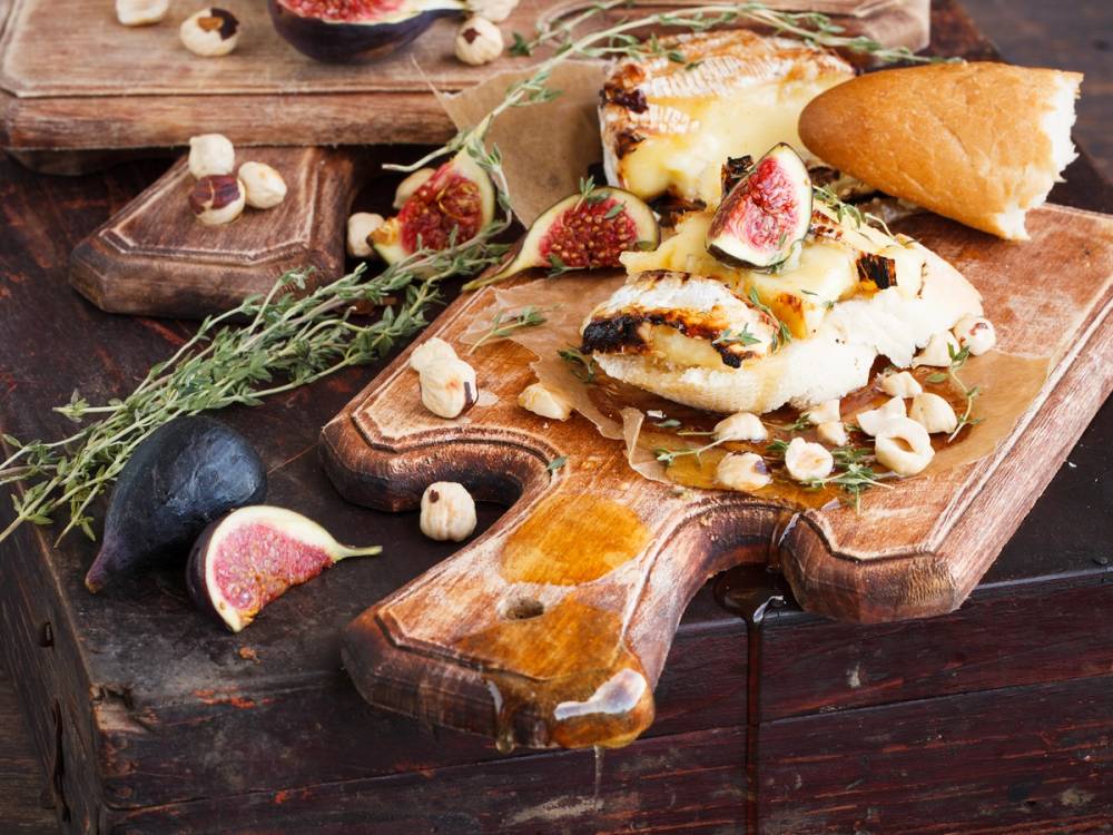 Ovnsbakt fransk camembert på et skjærebrett med fiken og urter rundt.