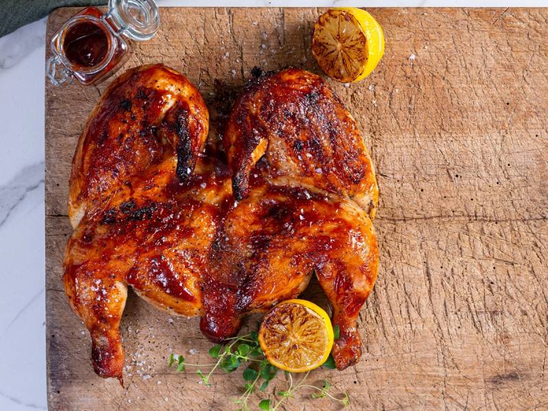 Tre grillede kyllinglår med sitronbåter og urter på et trebenet bord.