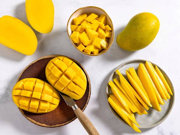 Ferske mangoer og mango i terninger på tallerkener og skåler, med en hel mango ved siden av.