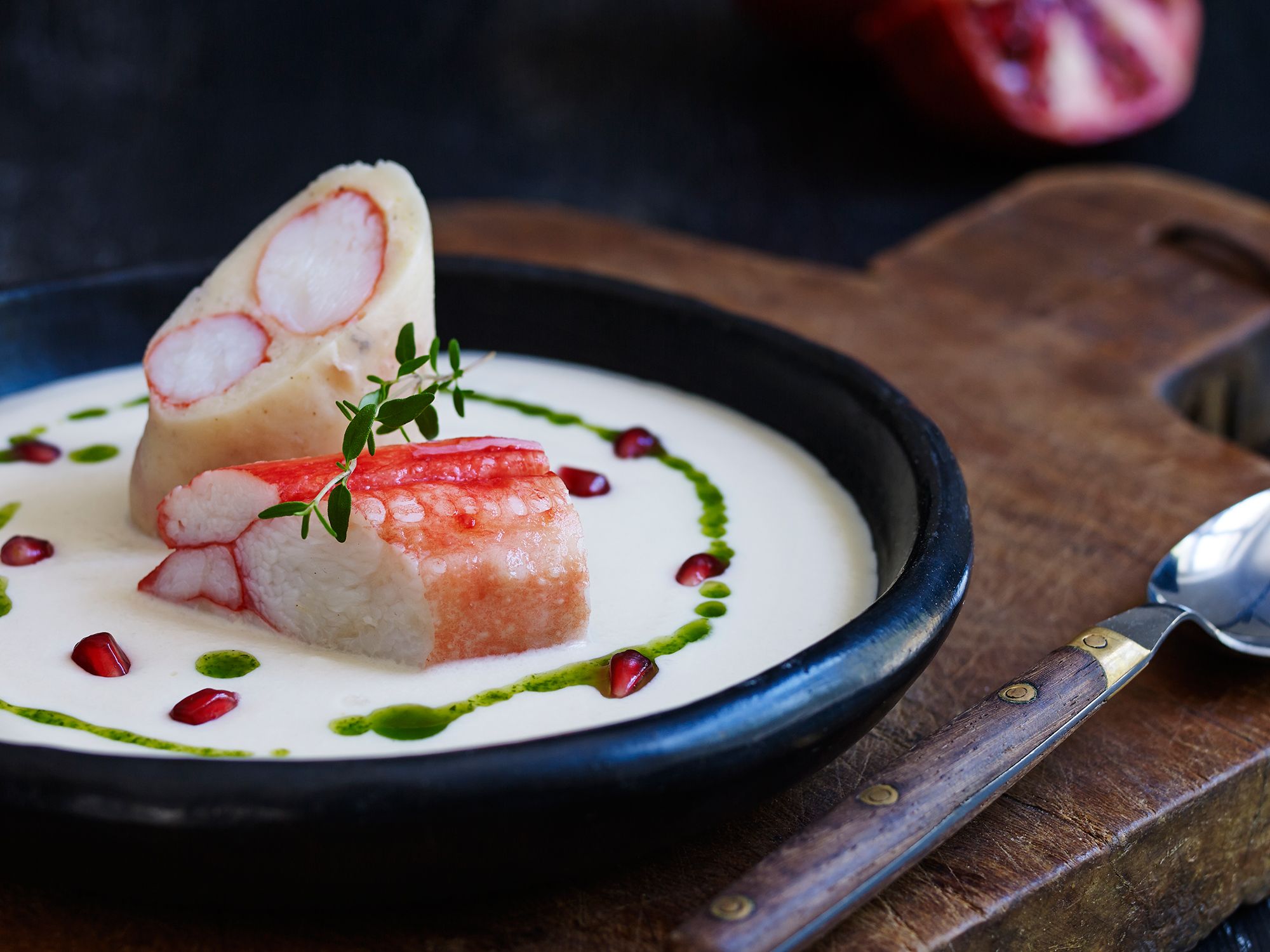 Kongekrabbe med jordskokksuppe servert i en svart bolle med pynt av urter og dråper av saus rundt.
