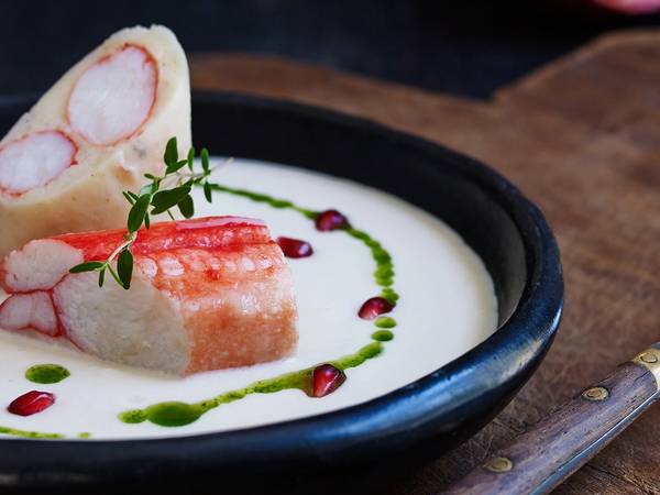Kongekrabbe med jordskokksuppe servert i en svart bolle med pynt av urter og dråper av saus rundt.
