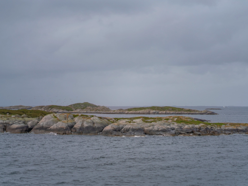 Utsikt over en kystlinje med steinete øyer under en overskyet himmel