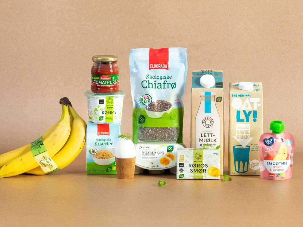 Økologiske matvarer og drikkevarer, inkludert bananer, yoghurt, melk og juice, er plassert på en hylle eller bord.