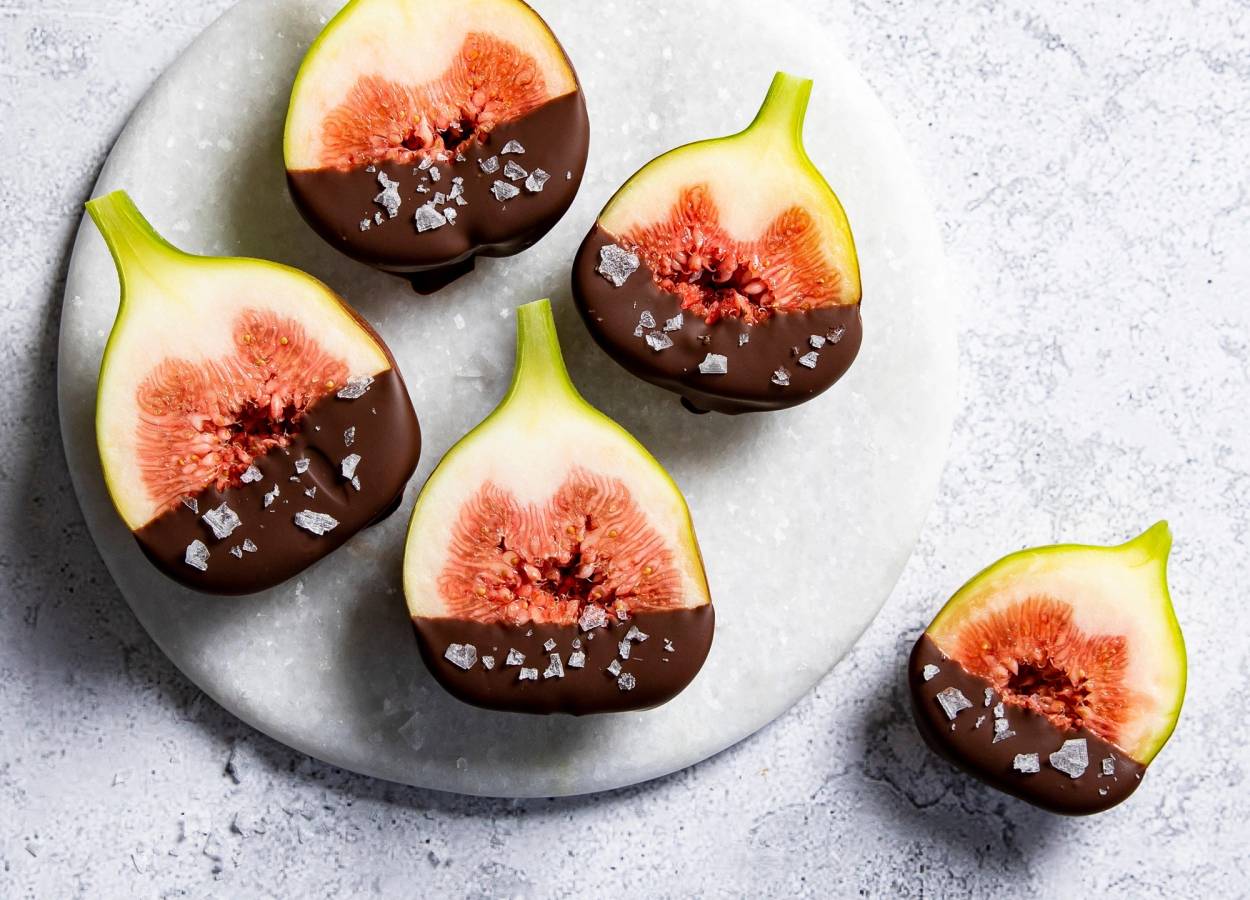 Ferske fiken dyppet i sjokolade med havsalt på en hvit tallerken.