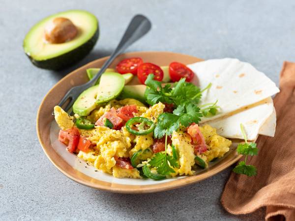 En tallerken med meksikansk eggerøre, avokado, cherrytomater, tortilla og frisk koriander, med en skje i midten.