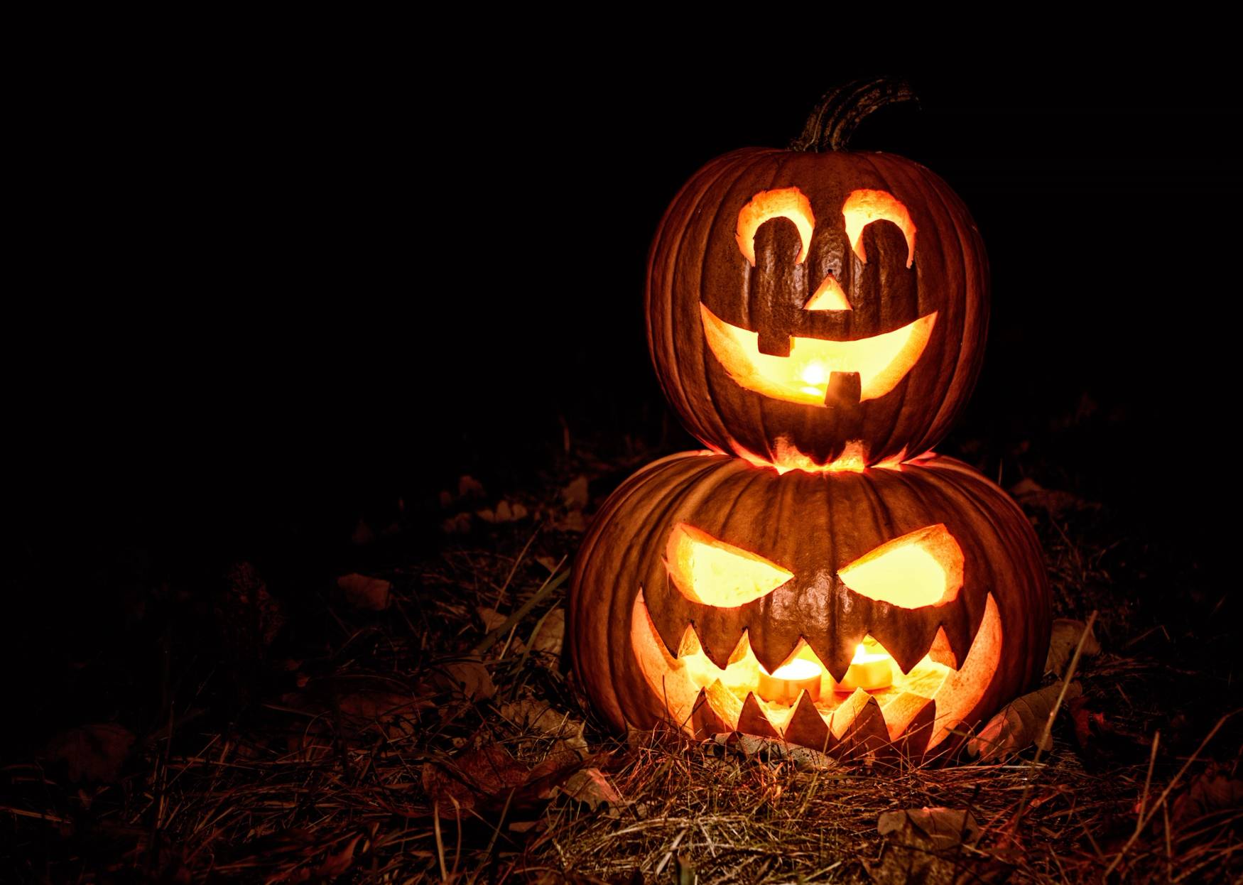 To opplyste halloween-pumpkiner med skumle ansikter i mørket, stablet oppå hverandre.