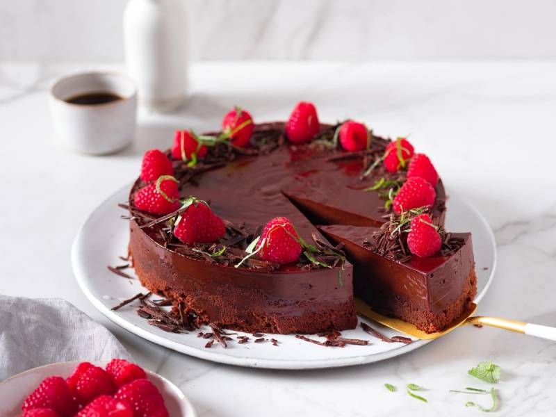 En sjokoladekake pyntet med friske bringebær og grønn pynt på en hvit tallerken.