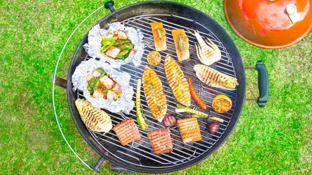 Grill med ulike typer fisk og skalldyr på en gressplen, klar til servering.