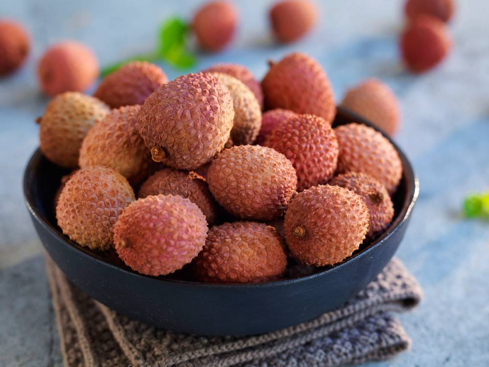 En skål med lyserøde litchi-frukter på en blå bakgrunn.