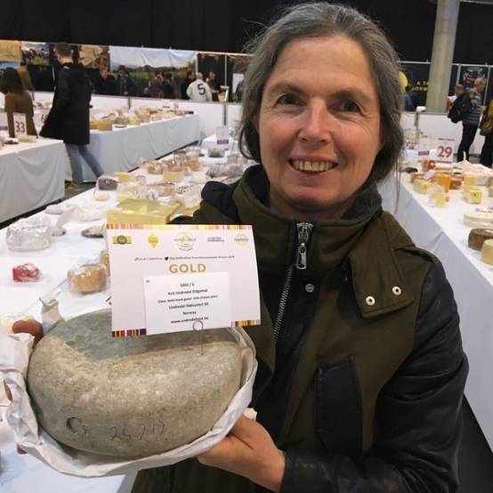 Person holder en stor ost med en gullmedalje på en utstilling eller marked.