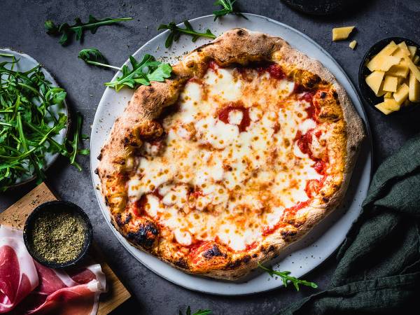 Margherita-pizza med ost, tomatsaus og basilikum på en tallerken, omgitt av urter og ingredienser.