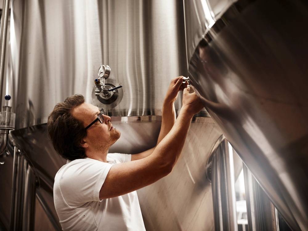 En person som jobber med å rengjøre innsiden av en stor, rund metallkonstruksjon, muligens en stor klokke, i et rom med lyse gardiner.
