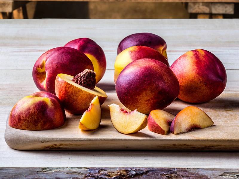 Ferskener og nektariner på et trestykke, noen skåret opp for å vise innmaten, på en lys treflate.