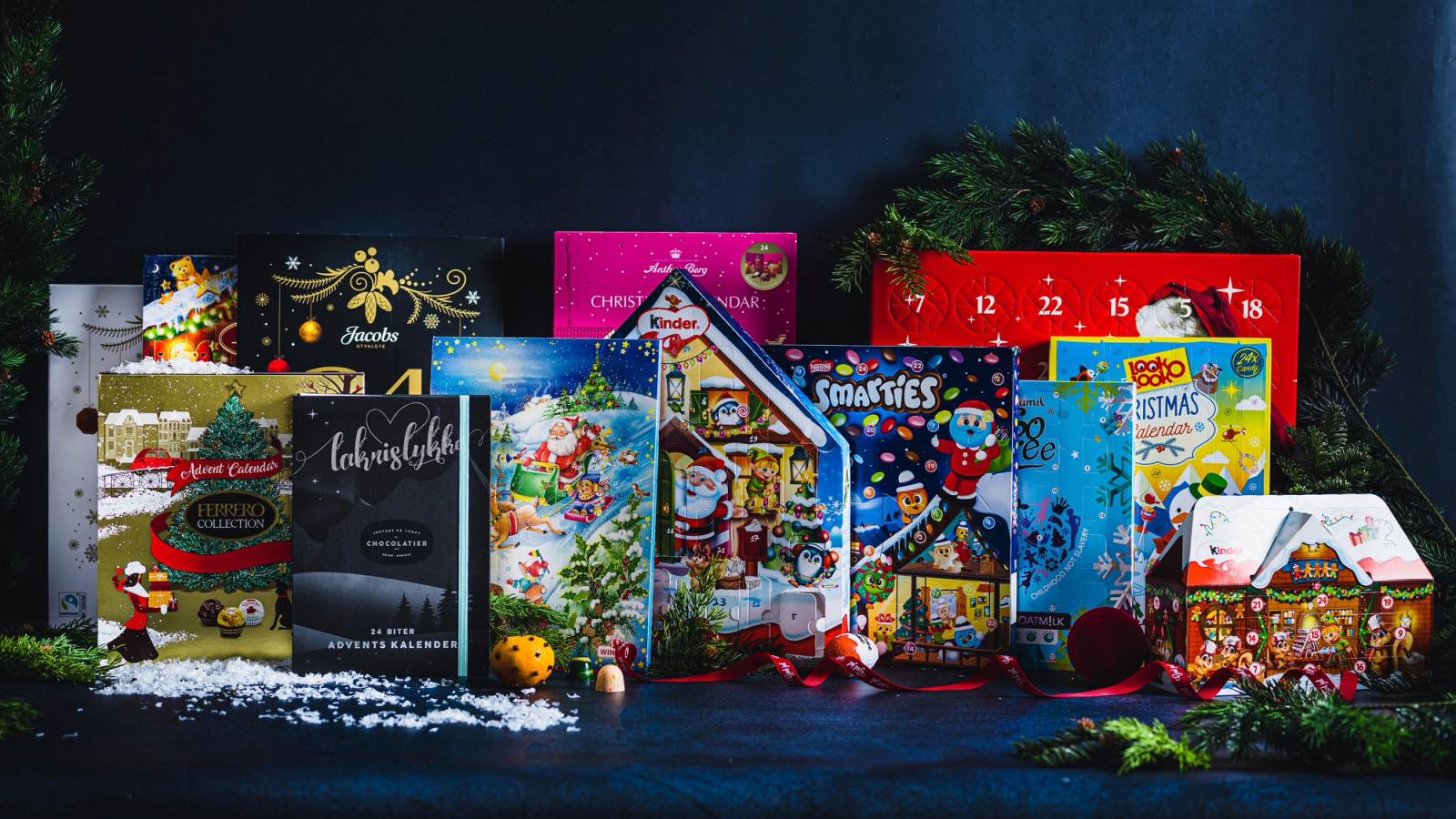 Flere kalendere for 2022 med jule- og vintermotiver, plassert på en mørk bakgrunn med granbar og julepynt rundt.