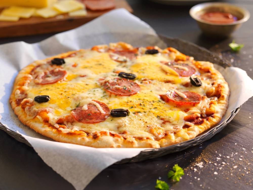 Pizza med chorizo, cheddarost og vellagret Valdresost på en svart stekeplate med en liten skål med saus i bakgrunnen.