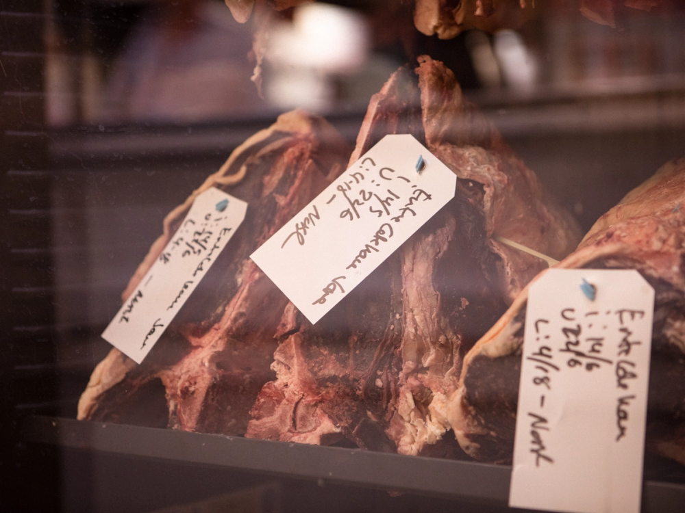 Ulike tørkede kjøttstykker med merkelapper i et kjøttskap for tørket modning av kjøtt, kjent som dry aged skap.