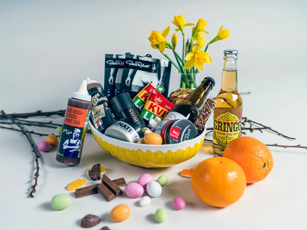 Påskeegg og sjokolade i en skål med to appelsiner og en flaske med påskegodt på et bord.