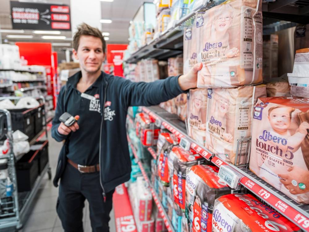 En person i butikkhylle med bleiepakker, som peker mot en eske med Libero bleier.
