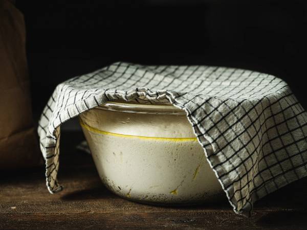 Deig som hever under et kjøkkenhåndkle i en bolle på et bord.