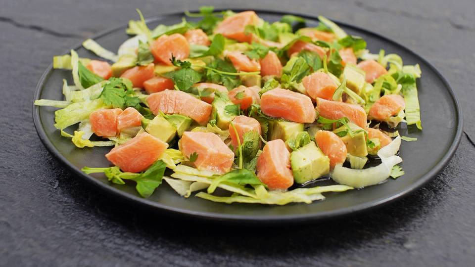 Laks ceviche med avokado og grønnsaker på en svart tallerken