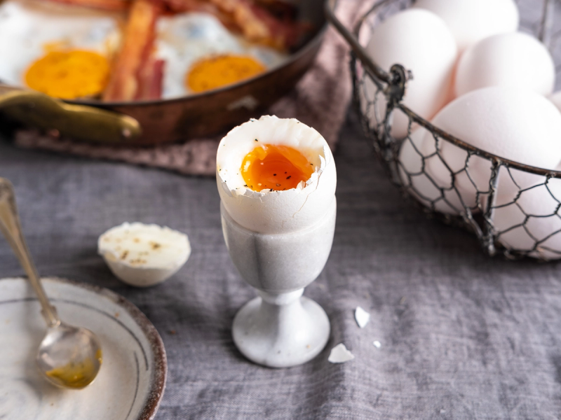 Et glass med et kokt egg med flytende eggeplomme på toppen, omgitt av flere hele egg i en kurv.
