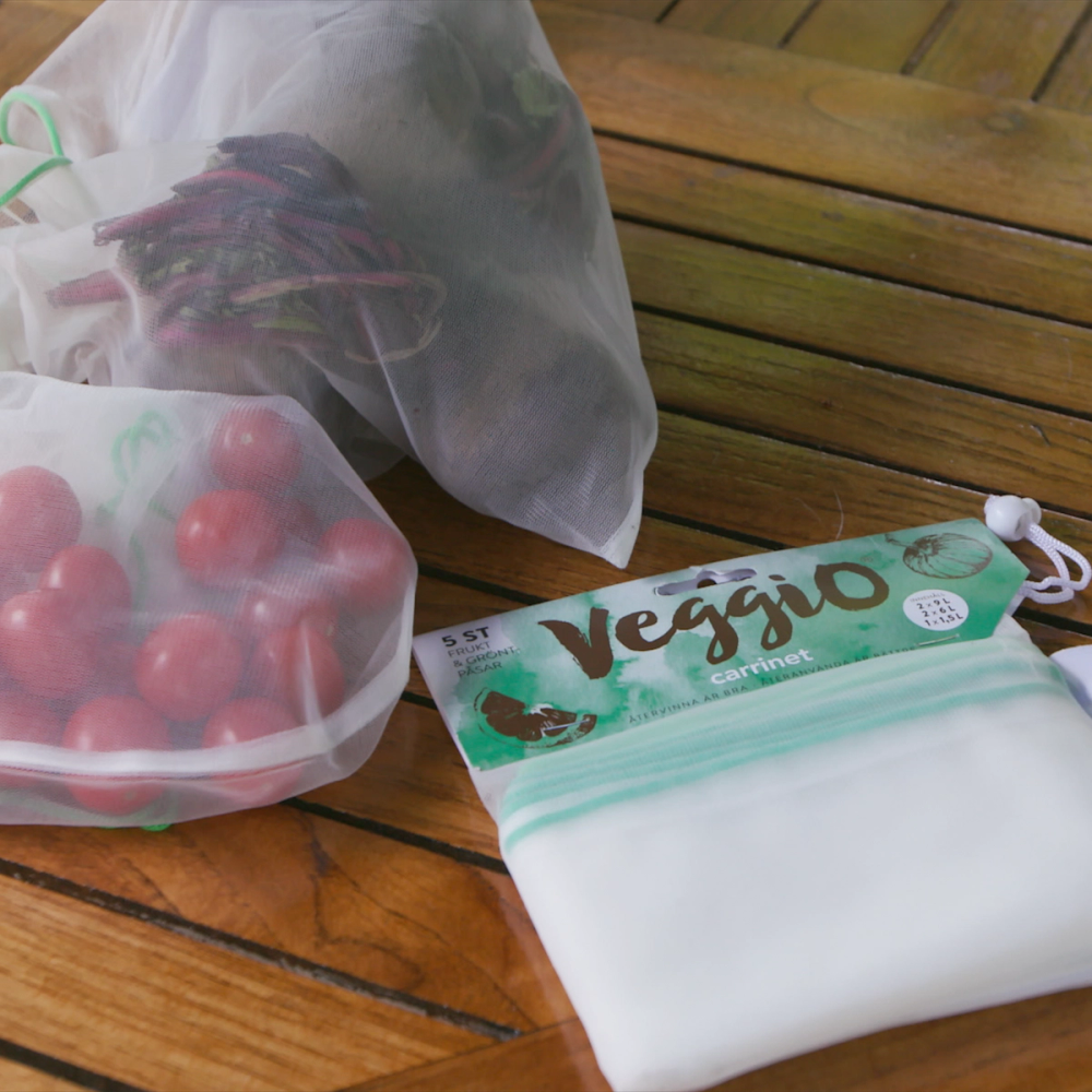 En gjenbrukspose med grønne og hvite farger ligger på et trebord, med en plastpose med tomater og en annen pose ved siden av.