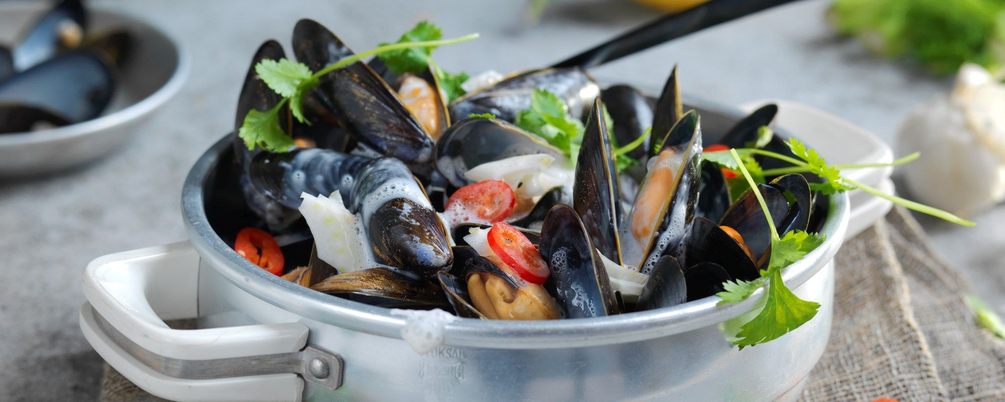 Asiatiske blåskjell i en hvit bolle med urter og grønnsaker, klar til servering.