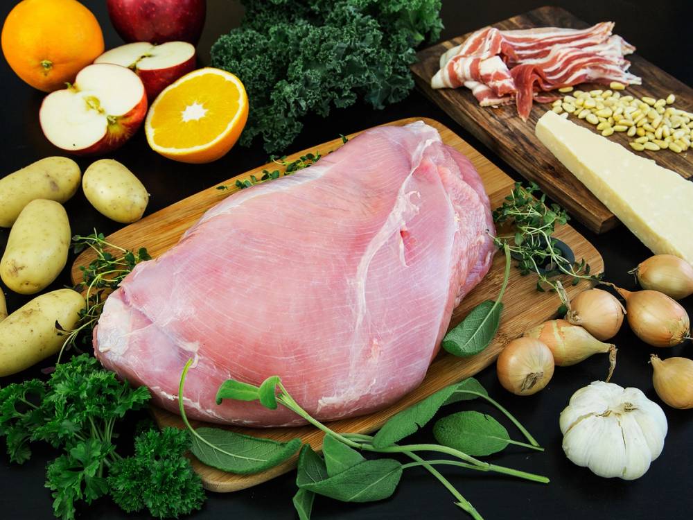 En rå kalkunfilet ligger på et skjærebrett omgitt av grønnsaker og andre matvarer.