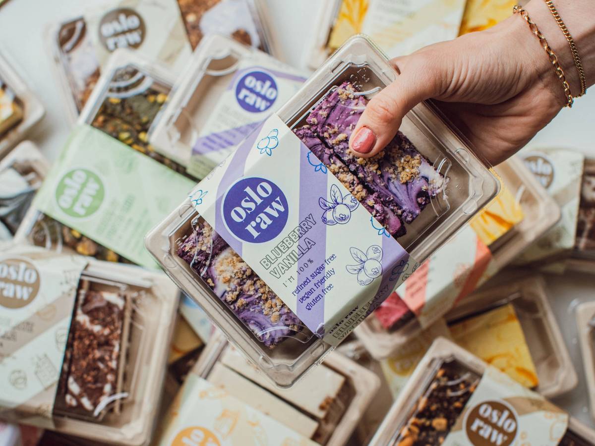 En hånd holder en eske med Oslo Raw-kaker blant flere andre kaker i bakgrunnen.