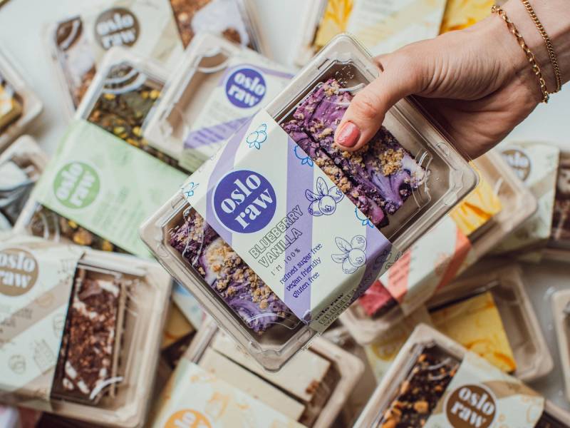 En hånd holder en eske med Oslo Raw-kaker blant flere andre kaker i bakgrunnen.