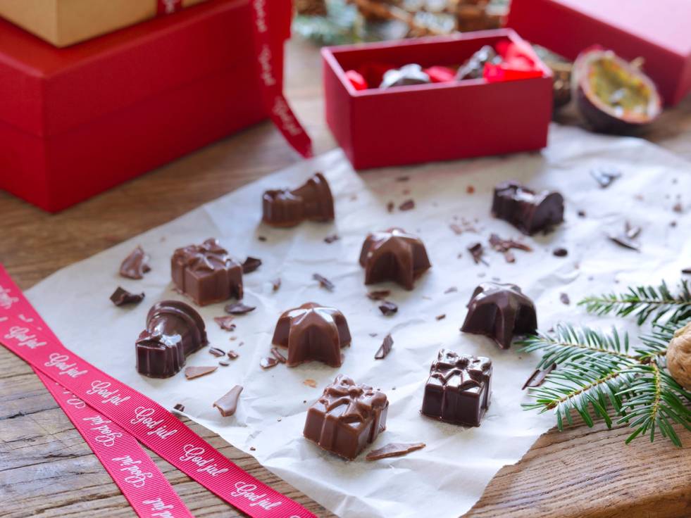 Ulike typer sjokolade- og konfektbiter ligger på et stykke hvitt papir, med en rød juleeske i bakgrunnen.