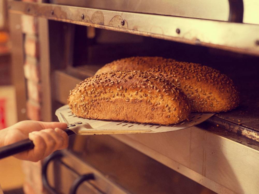 En person tar ut et halvstekt brød fra en ovn med en tang, klar til å stekes videre.