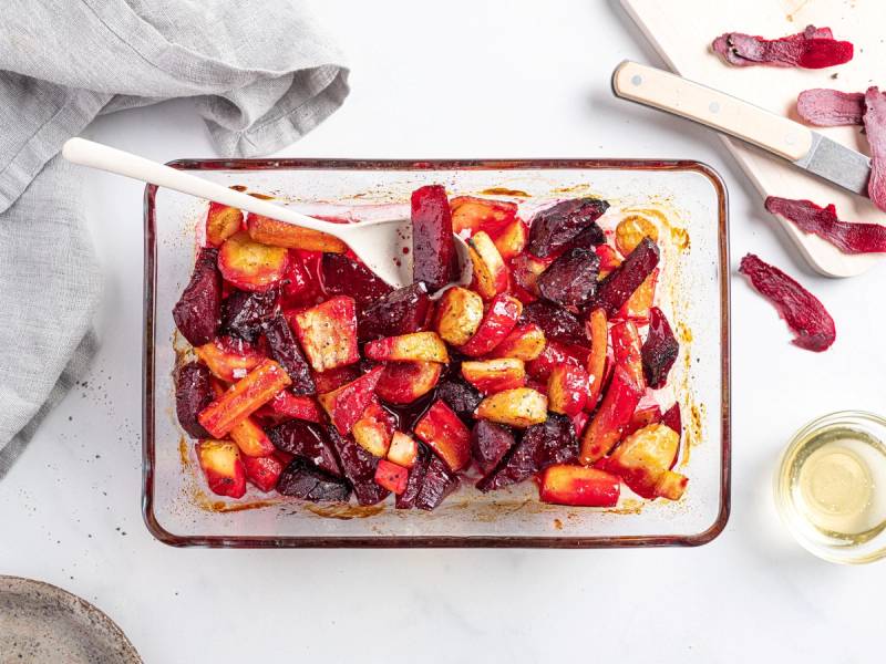 Honningglaserte rotgrønnsaker og beter i en ildfast form med en skje og noen skiver bete på siden