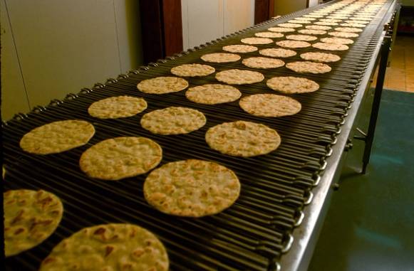 Rundkaker blir bakt på et samlebånd i en fabrikk, med flere kaker som beveger seg langs linjen.