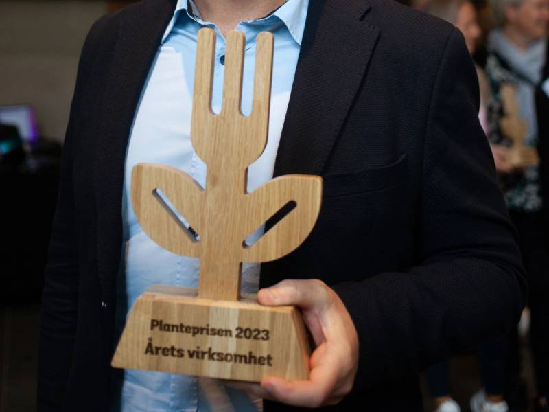 Person i dress holder opp en plantepris med teksten 'Planteprisen 2023 Årets virksomhet' på, under en taklampe.