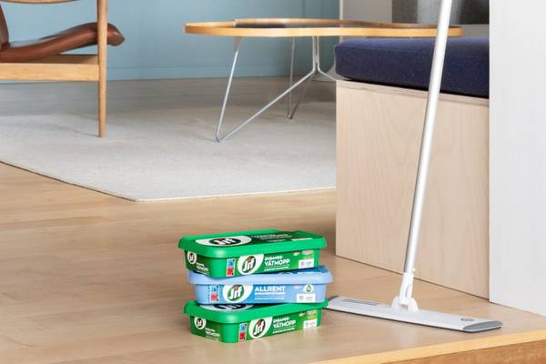 Jif gulvrengjøringsprodukter stablet på gulvet i et rom med lys tre- og hvite møbler.