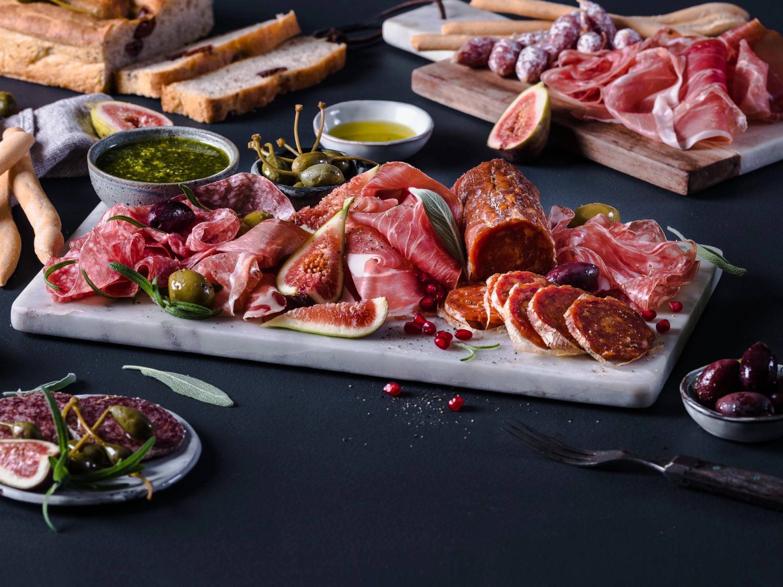 Spekemat med ulike typer kjøtt, pølser og tilbehør på et serveringsfat, med små skåler med saus og grønnsaker rundt.