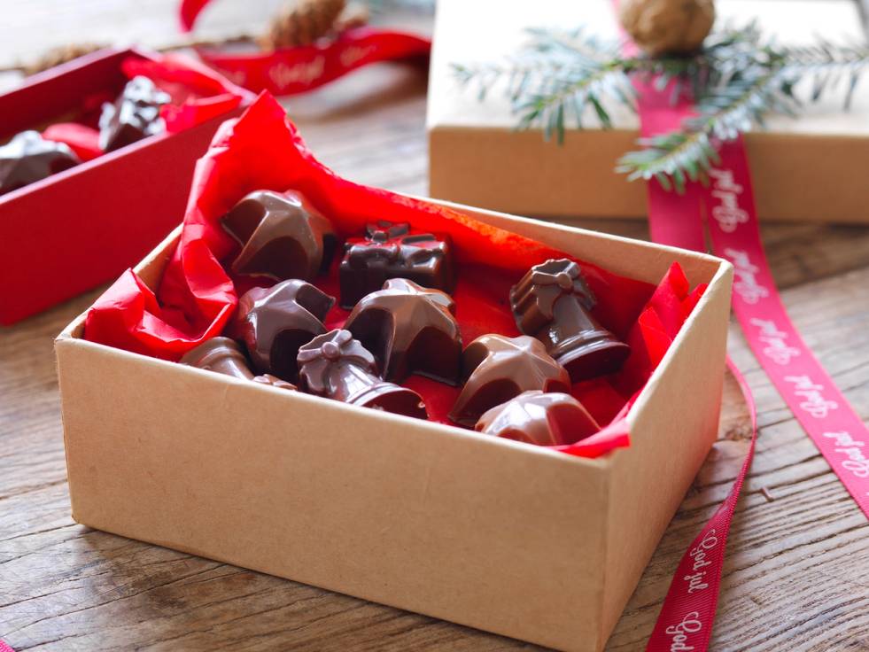 En eske med julekonfekt fylt med ulike sjokoladebiter, pyntet med rødt silkepapir og juledekorasjoner rundt.