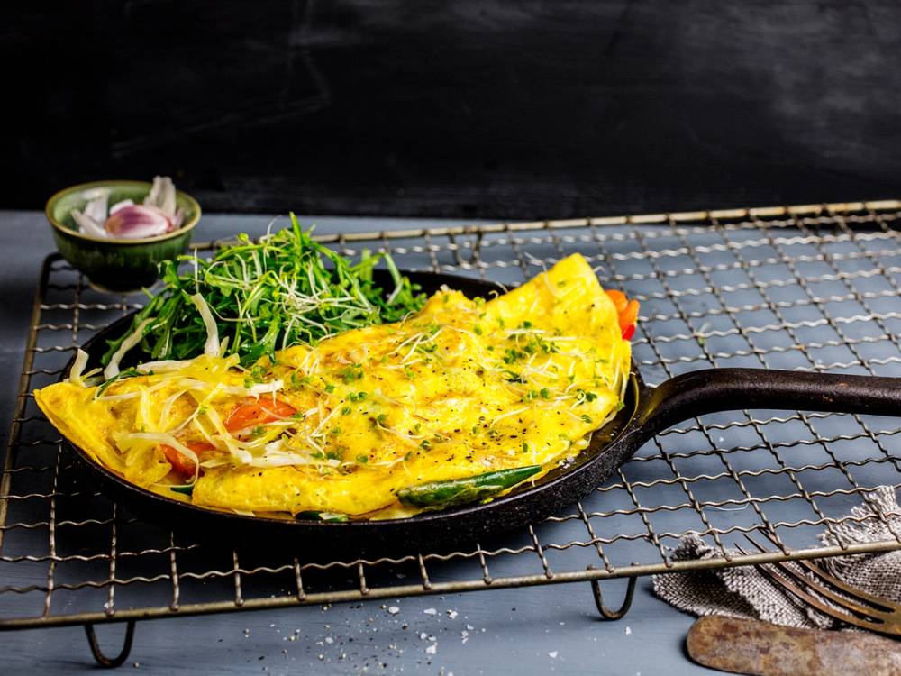 Stekt ris med omelett og grønnsaker på en svart stekepanne, plassert på et metallrist.