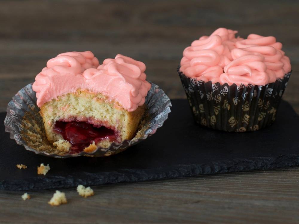 En cupcake med rosa krem og en hjerneformet dekorasjon på toppen, med en del av kaken som er tatt ut og viser fyll inni.