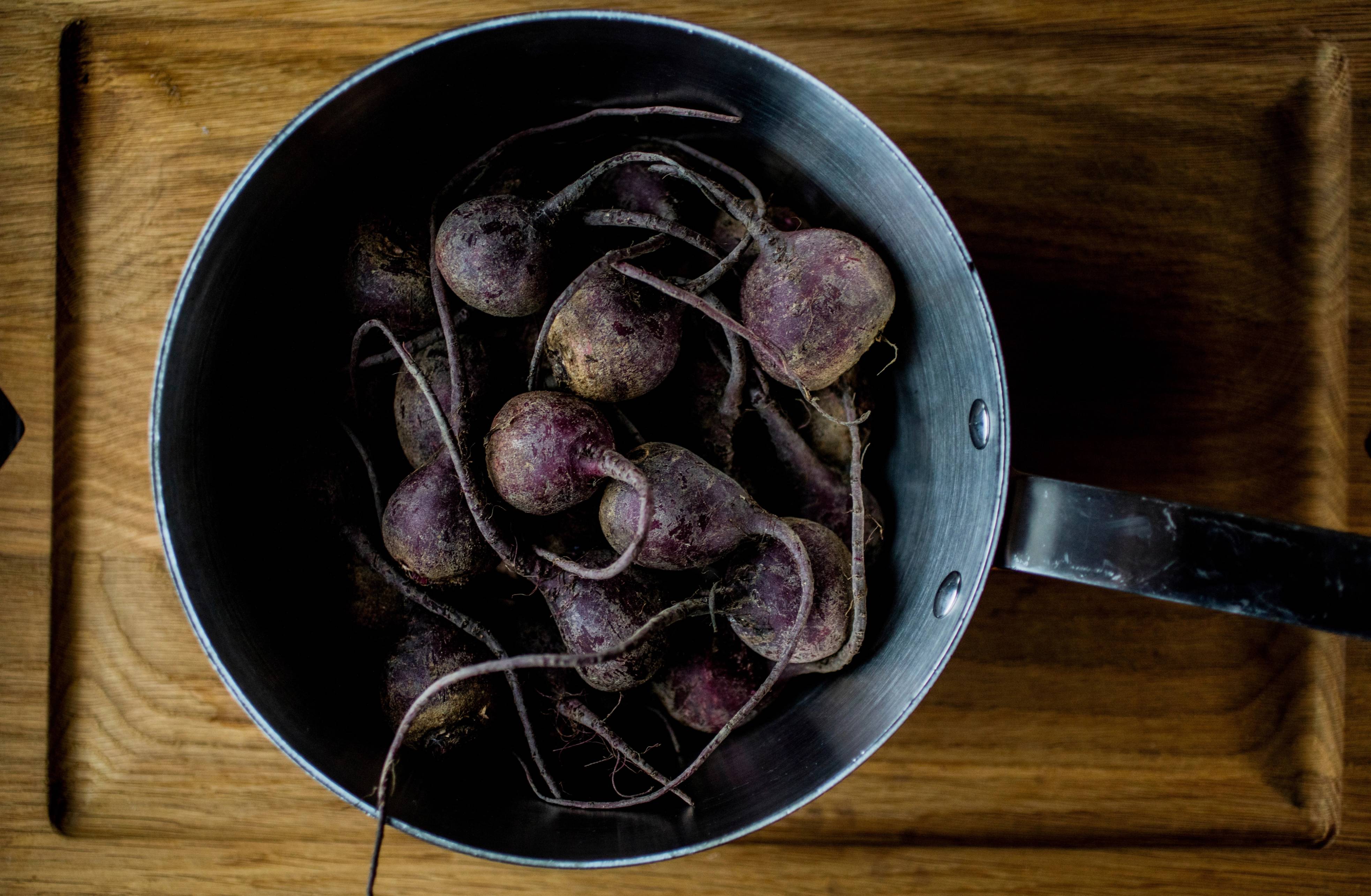 En panne med flere små, runde, lilla rotgrønnsaker, sannsynligvis jordskokk, på et treverkebord.