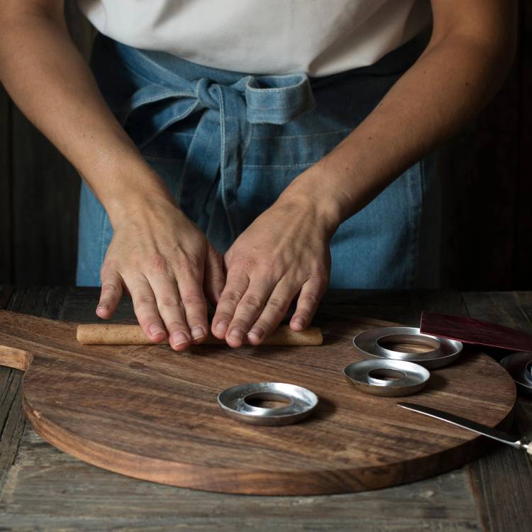 En person som baker kransekakeformer, med tre runde former og en kjevle på et rundt treplate.