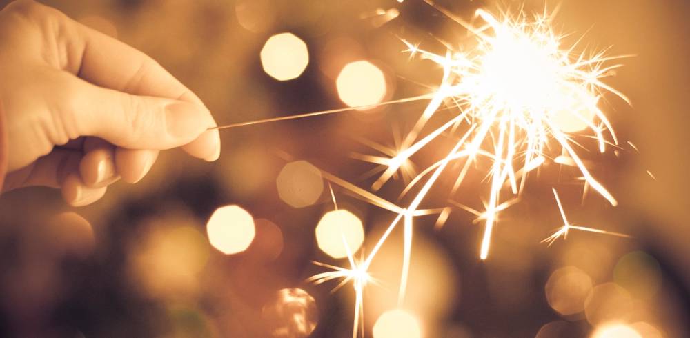 En person holder en brennende fakkel med fyrverkeri som lyser opp i bakgrunnen, sannsynligvis under nyttårsfeiring.