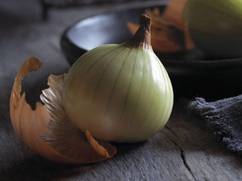 En hel løk med papirtynt skall ligger på en treoverflate, med en del av skallet løsnet ved siden av.