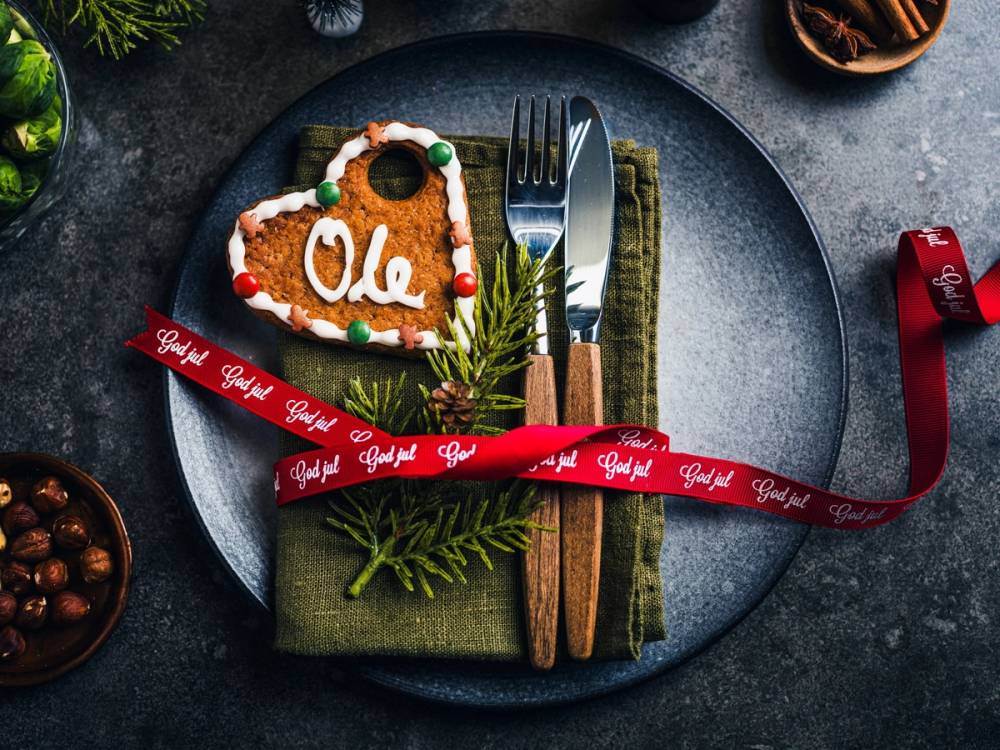 Et julebordkort med navnet Ole pyntet med pepperkake og grønn kvist på en tallerken, omgitt av julepynt og bestikk.