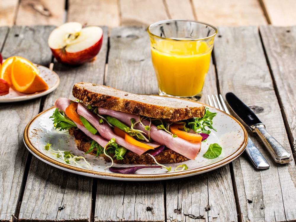 En full frokost med en skive brød med pålegg, et glass appelsinjuice og en skive eple på et treplatebord.