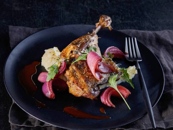 Andeconfit servert med rødløk og grønne urter på en svart tallerken